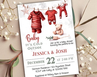 May include: A white baby shower invitation with a red and white striped baby outfit, a red baby onesie, a red and white star, and a teddy bear hanging on a clothesline. The text reads "Baby It's Cold Outside Jessica & Josh December 22 at 2:00 PM Dennison Residence 123 Anywhere Street RSVP with Kathy at 123.456.7890 Registered at Pottery Barn & Amazon"