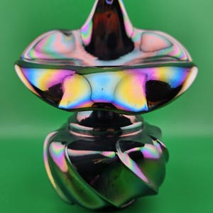 May include: Iridescent glass vase with a flared top and a bulbous, swirled base. The vase reflects a spectrum of colors, including pink, yellow, blue, and green, against a green background. The decorative piece has a unique, artistic design.