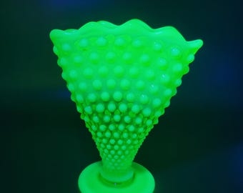 May include: A bright neon green hobnail glass vase with a flared, ruffled rim. The vase has a conical shape and sits on a round base. The hobnail texture covers the entire surface of the vase.