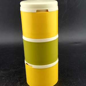 Puede incluir: Un recipiente de almacenamiento de alimentos de tres niveles. Las secciones superior e inferior son amarillas, y la sección media es verde oliva. Cada sección está separada por una banda blanca. La tapa es blanquecina.