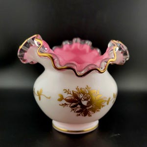 Può includere: Un vaso di vetro di latte bianco con un bordo superiore a balze rosa e un motivo floreale dorato.