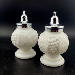 May include: A pair of white salt and pepper shakers with a grapevine design and silver tops.
