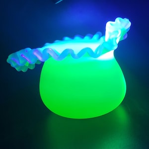 May include: A glowing green glass vase with a ruffled, wavy rim. The vase has a rounded shape and is illuminated with a bright green light, with a blue background. The rim is a lighter shade of green.