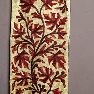 May include: A beige fabric wall hanging with a red and orange embroidered floral design.