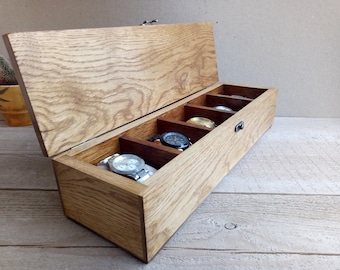 May include: A wooden watch box with a hinged lid and five compartments for storing watches. The box is made of light brown wood with a natural grain pattern. The lid is open and there are five watches inside the compartments.