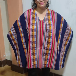 Peut inclure: Une femme portant un poncho rayé coloré avec une bordure bleu marine. Le poncho a un motif géométrique et est fait de tissu tissé.