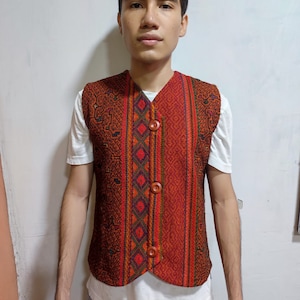 Könnte beinhalten: Eine Weste mit rotem, orangefarbenem, grünem und schwarzem Muster und Holzknöpfen.