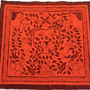 Pode incluir: Têxtil quadrado laranja com borda marrom escuro e design intrincado. A imagem central é um rosto de leopardo estilizado rodeado por folhas e figuras. A borda apresenta um padrão geométrico repetitivo.