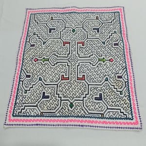 Könnte beinhalten: Quadratischer weißer Textilartikel mit einem komplexen geometrischen Muster in Schwarz, Blau, Rot, Grün und Rosa. Das Design zeigt ineinandergreifende Formen und Linien mit einem rosa Rand und blauen Nähten. Der Textilartikel ist wahrscheinlich handgefertigt.