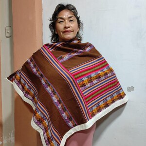 Peut inclure: Une femme portant un poncho brun avec des rayures colorées et des motifs géométriques. Le poncho a une bordure blanche. La femme porte un pantalon rose.