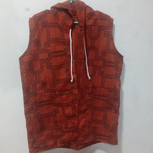 May include: A sleeveless hooded vest with a geometric pattern in shades of brown and black. The vest has a drawstring hood and a white drawstring.
