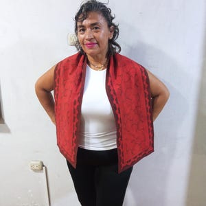 May include: A woman wearing a red and brown patterned scarf over a white shirt and black pants.