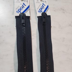 May include: Two black separating sport zippers by Coats & Clark, each measuring 30 inches in length. The packaging features white cards with blue and grey accents, displaying the brand name, the word sport, and the length in inches and centimeters.