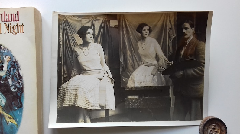 Puede incluir: Una fotograf&iacute;a en blanco y negro de una mujer posando para un retrato. La mujer lleva un vestido blanco y est&aacute; sentada en una silla. Un hombre est&aacute; de pie detr&aacute;s de ella, sosteniendo un pincel y una paleta.