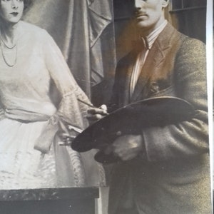 Puede incluir: Una fotograf&iacute;a en blanco y negro de un hombre sosteniendo una paleta de pintura y un pincel, de pie junto a una mujer con un vestido blanco. El hombre lleva una chaqueta de traje y una camisa con cuello. La mujer lleva un vestido blanco con un lazo en la cintura.