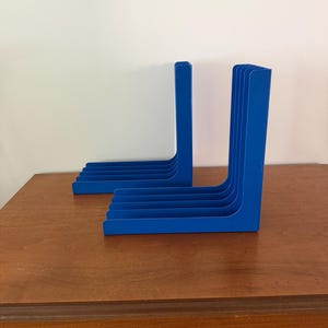 May include: Two blue L-shaped organizers, each featuring five parallel vertical slots. These solid blue units are constructed with a flat base and a tall upright section, designed to hold items in an upright position with a clean, uniform appearance.