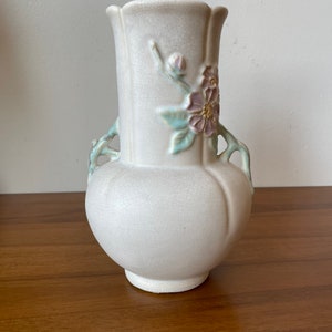 May include: A white ceramic vase with a floral design. The vase has two handles and a crackled glaze. The flowers are pink and green.