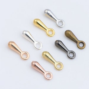 May include: Assortment of eight metal jewellery findings in various colours, including silver, gold, bronze, and black. Each finding has a teardrop shape with a loop at the end.