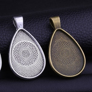 Könnte beinhalten: Drei silberne und bronzene Anhänger-Tabletts in Tropfenform mit einem dekorativen Muster. Die Tabletts sind so konzipiert, dass sie ein kleines Bild oder ein anderes dekoratives Element aufnehmen können.