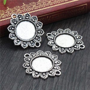 May include: Three silver-toned metal pendant charms with a floral design. Each charm has a round, empty space in the center for adding a cameo or other embellishment.