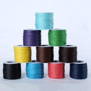 Könnte beinhalten: Eine Pyramide aus farbigen Wachskordelspulen. Die Farben umfassen Schwarz, Blau, Rot, Gelb, Grün, Braun und Lila. Jede Spule ist fest gewickelt und sitzt auf einer weißen Kunststoffbasis. Für Schmuckherstellung und Bastelarbeiten.