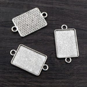 May include: Three silver-toned metal rectangular frames with jump rings. The frames are blank and ready for crafting.