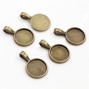 May include: Five antique bronze pendant trays with a round shape and a smooth, slightly textured surface. The trays have a loop at the top for attaching to a chain or cord.
