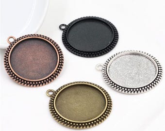 Op de afbeelding: Vier metalen bezel hanger trays in koper, zwart, zilver en antiek messing. Elke tray heeft een ronde, getextureerde rand en een lus om aan een ketting of koord te bevestigen. Ideaal voor het maken van sieraden.