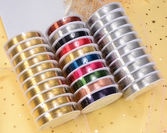 Puede incluir: Surtido de carretes de alambre de colores y metálico para la elaboración de joyas. Los carretes están dispuestos en una fila sobre una superficie amarilla con purpurina dorada.