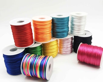 May include: Assortment of colorful spools of thread, including red, orange, yellow, green, blue, pink, white, and black. The spools are arranged in a semi-circle on a white surface.