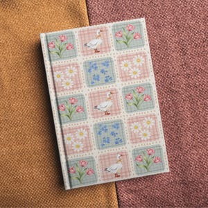 May include: A rectangular hardback notebook featuring a repeating grid pattern of squares. The design includes illustrations of white geese with yellow ribbons, pink tulips, white daisies, and small blue flowers on alternating pastel backgrounds.