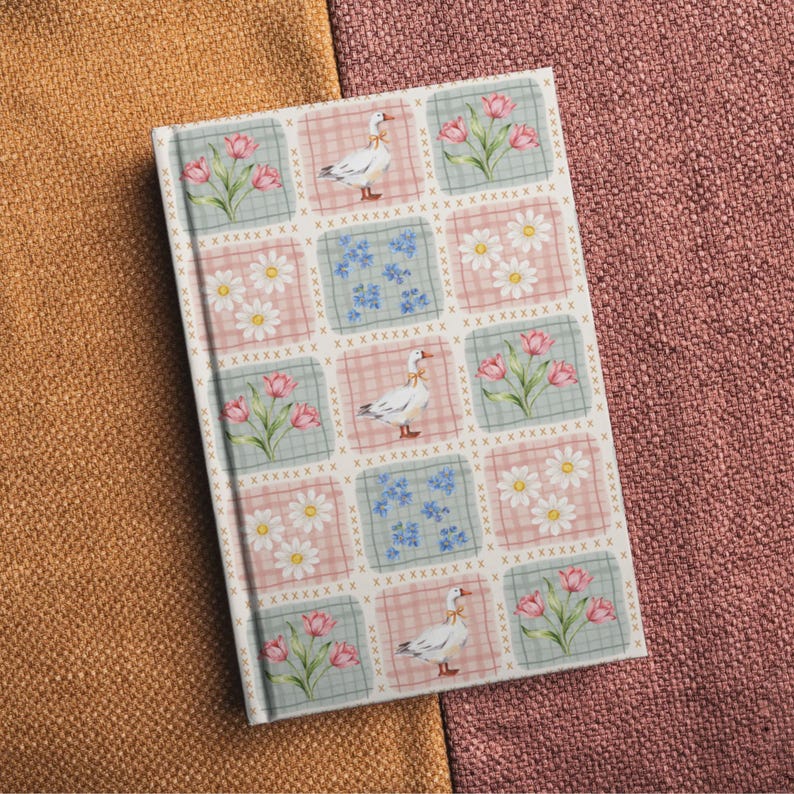 May include: A rectangular hardback notebook featuring a repeating grid pattern of squares. The design includes illustrations of white geese with yellow ribbons, pink tulips, white daisies, and small blue flowers on alternating pastel backgrounds.