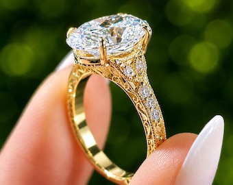 Könnte beinhalten: Ein Ring aus Gelbgold mit einem großen oval geschliffenen Mittelstein und einer Ringschiene mit filigranen Metallarbeiten. Die Schiene ist mit kleinen rund geschliffenen Steinen an den Seiten besetzt, die eine detaillierte Verarbeitung zeigen.