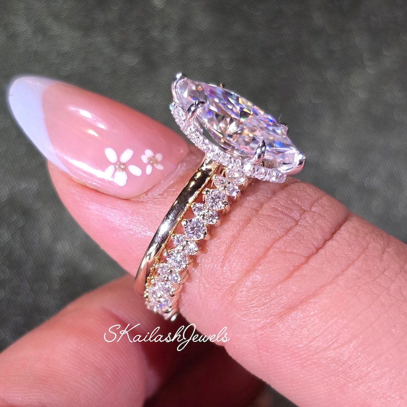 May include: A marquise-cut diamond engagement ring with a halo setting, paired with a diamond band. The rings are gold and feature numerous small, round diamonds. The image includes the text "Skailash Jewels".