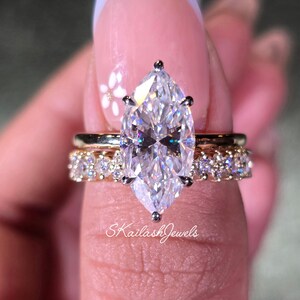 May include: A marquise-cut diamond engagement ring with a gold band, set with smaller diamonds. The ring is paired with a gold band with small diamonds. The text "SKailashJewels" is visible.