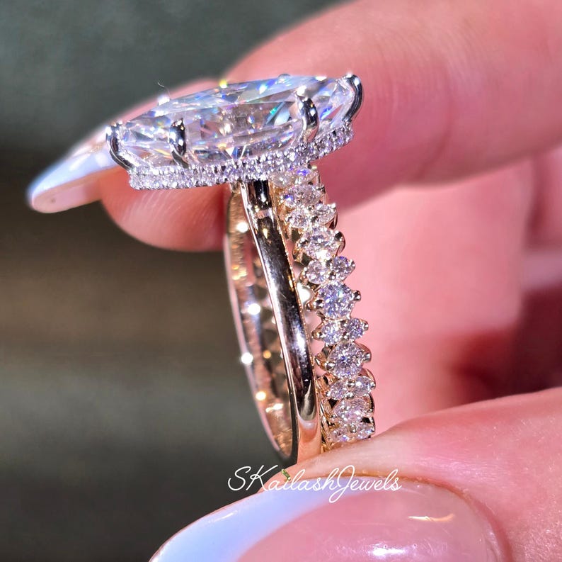 May include: A close-up of two rings. The engagement ring features a large, clear, marquise-cut stone with a halo of smaller stones. The wedding band is a gold band with small, round stones. The text "SKailashJewels" is visible.