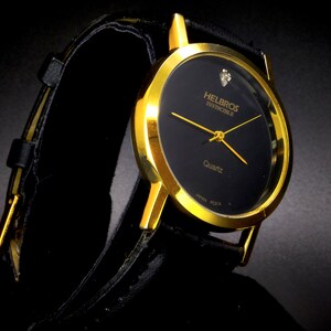 May include: A gold-tone wristwatch with a black face and a black leather band. The watch face has the words "Helbros Invincible" and "Quartz" printed on it.