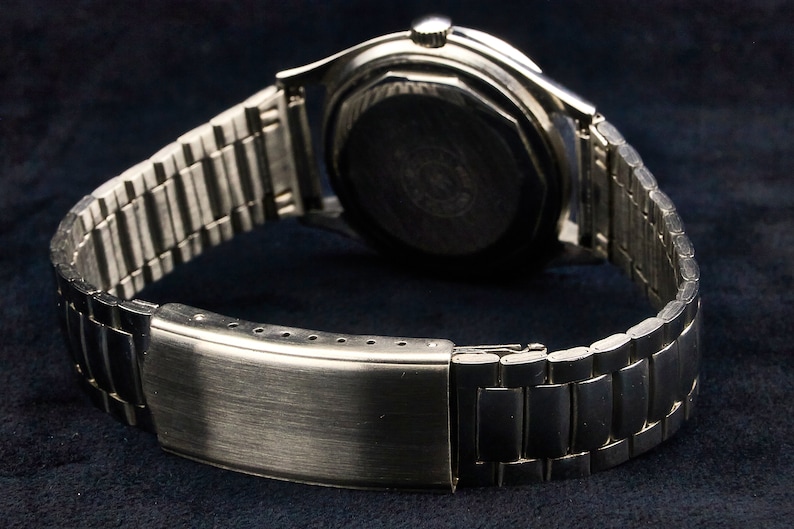 May include: A silver wristwatch with a metal band. The watch face is not visible, but the back of the watch is visible.
