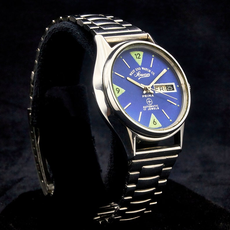 May include: A silver Prima automatic watch with a blue face and a silver band. The watch face has white markings and a date window that says "FRI 25". The watch also has the text "West End Watch Co. London" and "Automatic 17 Jewels".