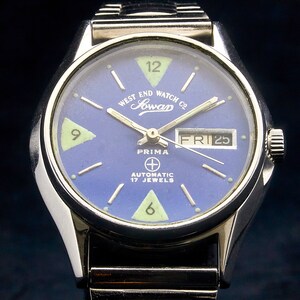 May include: A silver wristwatch with a blue face and white markings. The watch face has the text "West End Watch Co. Jowan Prima Automatic 17 Jewels" and the date "FRI 25".