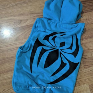 Puede incluir: Una sudadera azul sin mangas con un dise&ntilde;o de telara&ntilde;a de ara&ntilde;a negra en la espalda. La sudadera tiene capucha y cremallera. El texto "Iwan Zona Kaos" est&aacute; impreso en la parte inferior de la sudadera.