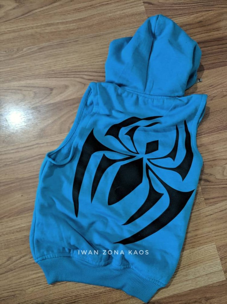 Puede incluir: Una sudadera azul sin mangas con un dise&ntilde;o de telara&ntilde;a de ara&ntilde;a negra en la espalda. La sudadera tiene capucha y cremallera. El texto "Iwan Zona Kaos" est&aacute; impreso en la parte inferior de la sudadera.