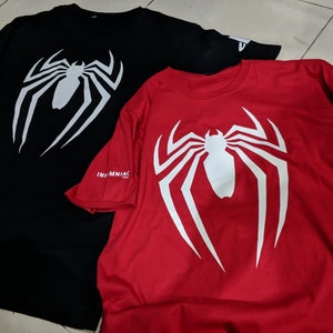 May include: Two t-shirts with a white spider-man logo on the front. The shirt on the left is black and the shirt on the right is red. Both shirts have the word "Insomniac" printed on the sleeve.