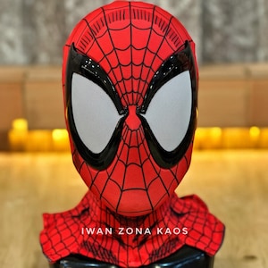 Op de afbeelding: Een rood Spider-Man masker met een zwart webpatroon en grote witte ooglenzen. Het masker heeft een zwarte rand rond de ogen en een nekstuk. De tekst "IWAN ZONA KAOS" is op de nek gedrukt.