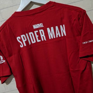May include: Red t-shirt with white text that reads "MARVEL SPIDER-MAN" and "INSOMNIAC GAMES" on the back. The PlayStation logo is on the left sleeve.