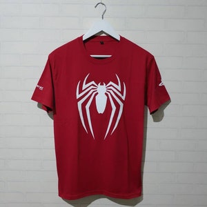 May include: Red t-shirt with a white spider-man logo on the front.