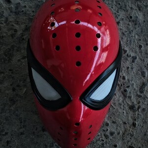 以下が含まれることがあります： 赤い黒のスパイダーマンマスク。メッシュアイデザインとテクスチャ加工された表面。マスクは、縁の周りに小さな穴がいくつかあり、あごに大きな穴があります。マスクの下部に「IWAN ZONA KAOS」というテキストが印刷されています。
