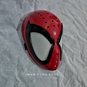 Op de afbeelding: Rood en zwart plastic Spider-Man-masker met een gaasoogbedekking. Het masker heeft een gestructureerd oppervlak en kleine gaatjes overal.