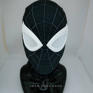 May include: Black and white Spider-Man mask with a black web pattern and white mesh eyes. The mask is on a black mannequin head with the text "Iwan Zona Kaos" on the base.