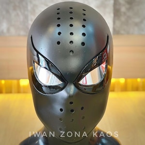 May include: A black mask with a design reminiscent of a superhero. The mask has reflective eye coverings and small ventilation holes. The text "IWAN ZONA KAOS" is visible at the bottom.